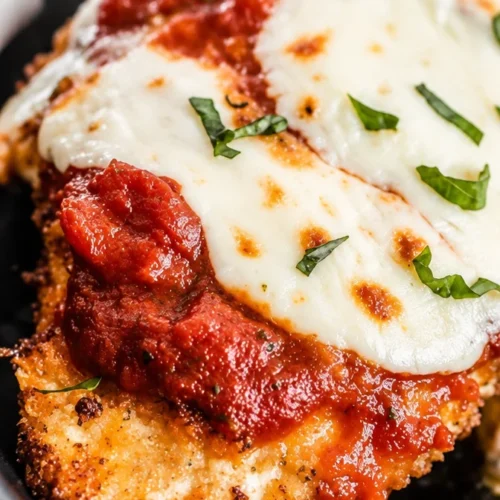 Easy baked chicken parmesan topped with fresh mozzarella and basil on a plate
